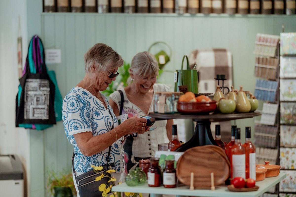 To kvinner ser på varer i en museumsbutikk som bugner av servietter, blomsterpotter og andre hageartikler.